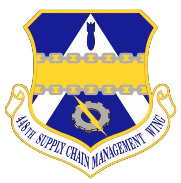 Ein Schild mit einem blauen Hintergrund, einem weißen Stern in der Mitte und einem weißen Banner mit der Aufschrift "Supply Chain Management" in blau, umgeben von einem weißen Rand, mit der schwarzen, fetten Schrift "48th Supply Chain Management Wing" darüber und darunter.