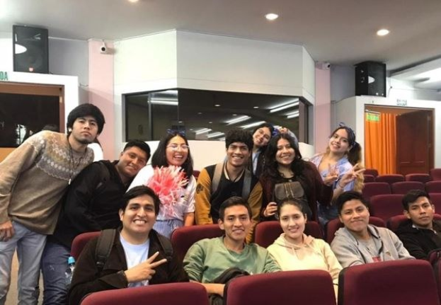 Gruppe von lachenden Menschen, die für ein Foto in einem Kino posieren, mit Lautsprechern an der Wand und Deckenlampen, aufgenommen auf einem Filmfestival.