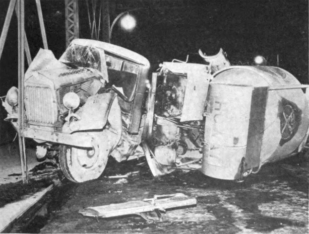 Ein Schwarz-Weiß-Foto eines umgestürzten Autos aus den 1930er Jahren änd der Straßenseite mit Metallstäben und einer Laterne im Hintergrund.