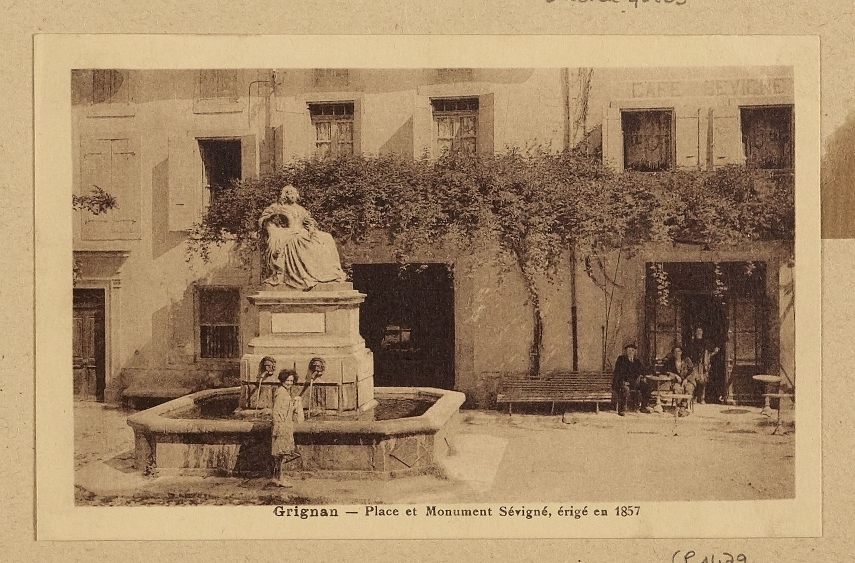 Ein altes Foto eines Brunnens mit einer Statue auf einem Sockel in der Mitte, umgeben von Menschen, die auf Bänken sitzen, mit einem Baum im Hintergrund und Text unten.