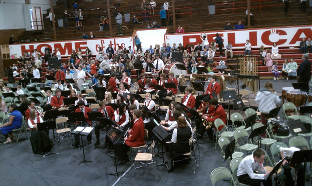 Eine Gruppe von Kindern sitzt auf Stühlen in einem Stadion für eine Musikstunde, mit Stadionplätzen im Hintergrund.