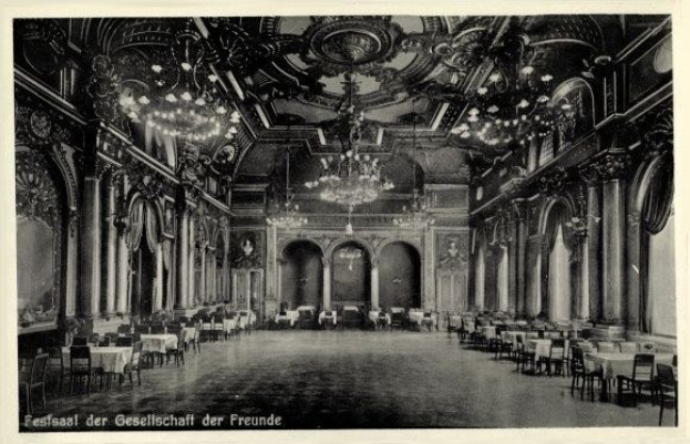 Schwarzes und weißes Foto einer großen Halle mit Reihen von Tischen und Stühlen, tragenden Säulen, gewölbten Decken und prunkvollen Kronleuchtern, mit der Aufschrift "Festival der Gesellschaft der Freunde, Berlin" unten.