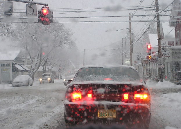 Eine schneebedeckte Straße mit Häusern und Bäumen auf beiden Seiten und wenigen Fahrzeugen.