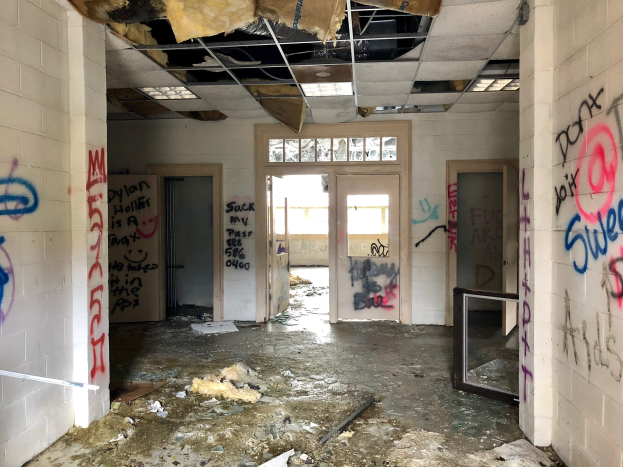 Verlassene Gebäude mit Graffiti-verschmierten Wänden und Decke, Schutt auf dem Boden, mehrere Türen und Fenster im Hintergrund und verstreute Gegenstände.
