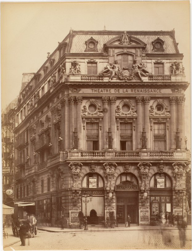 Schwarz-weißes Foto des Théâtre de la Renaissance in Paris, das eine Fassade mit Fenstern, Säulen, Bögen und Skulpturen zeigt, mit ein paar Menschen und Fahrzeugen auf der Straße davor und dem Himmel im Hintergrund.