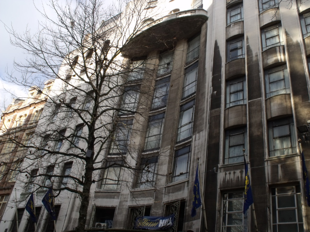 Gebäude mit Fenstern, eine Fahne und Flaggen an Stangen unten und einem Baum mit Zweigen.