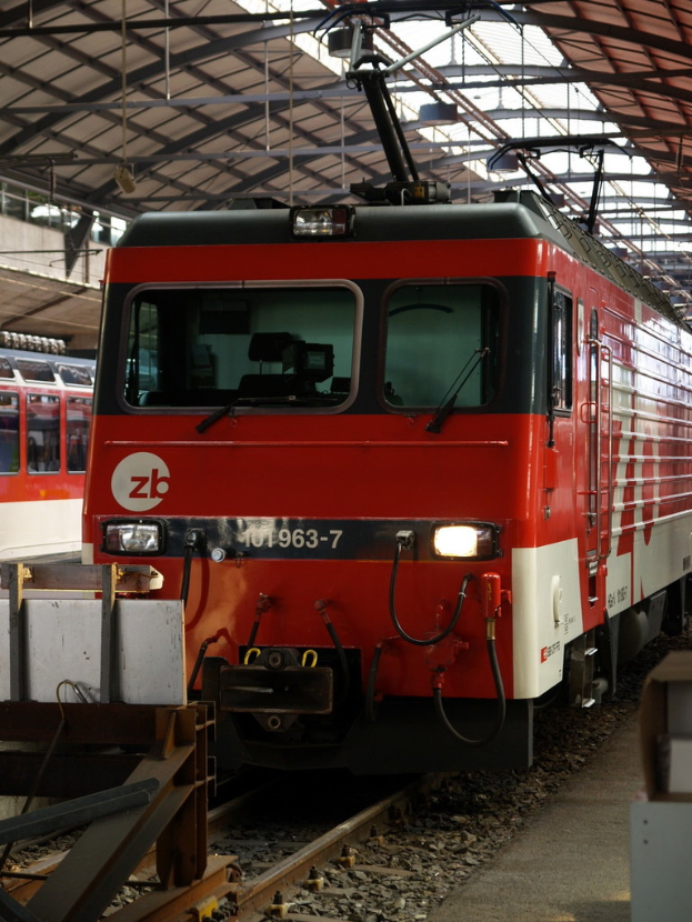 Ein Zug auf einem Bahngleis mit Steinen und Stangen in der Nähe und lesbarem Text auf dem Zug.