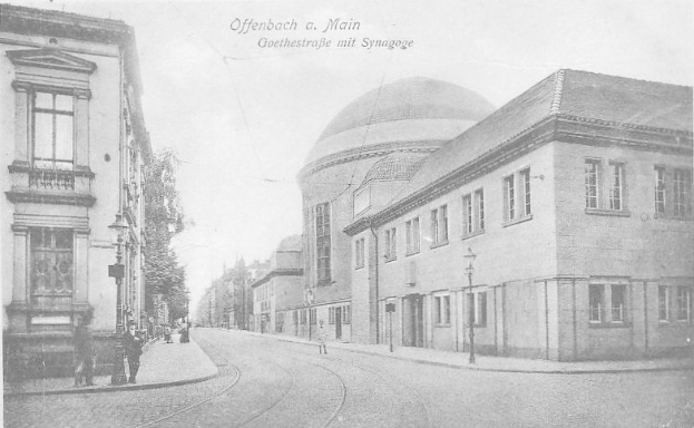 Ein Schwarz-Weiß-Foto einer Stadtstraße namens Goethestraße in Offenbach am Main, das Gebäude, Straßenlaternen, Straßenlaternen, Bäume und Menschen zeigt, die auf der Straße gehen, mit der Aufschrift "Offenbach a Main, Goethestraße mit Synagoge" oben.