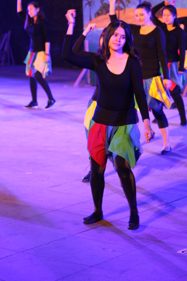 Gruppe junger Frauen, die auf der Bühne tanzen, mit einem Bild im Hintergrund, alle tragen Schuhe.