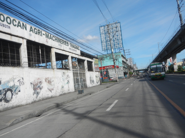 Eine Stadtstraße mit Fahrzeugen, einer Brücke, Gebäuden, Strommasten mit Kabeln, einem bewölkten Himmel und einem graffiti-beschmierten Gebäude an der Seite.