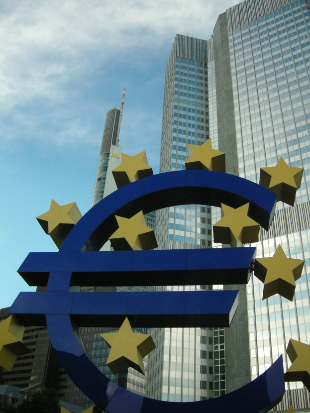 Euro-Zeichen vor dem Hauptsitz der Europäischen Zentralbank in Frankfurt, Deutschland, mit Bäumen und einem bewölkten Himmel.