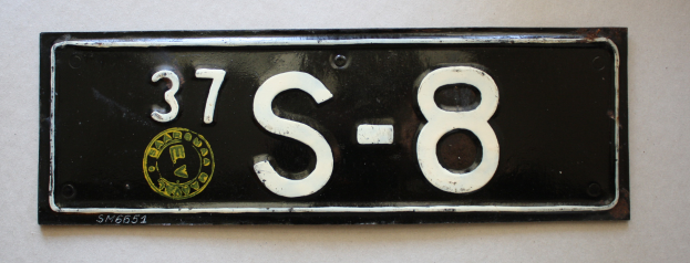 Ein schwarzes und weißes Kennzeichen mit der Nummer 37-8 auf einer weißen Wand montiert.