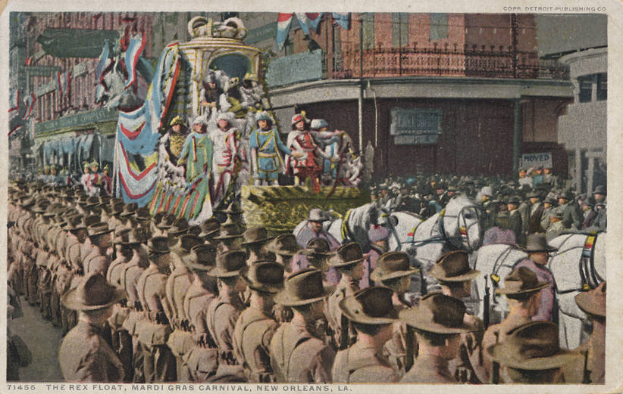 Eine alte Postkarte zeigt einen Mardi Gras-Umzug in New Orleans mit einem Schmuckfloß, Reiter und Zuschauern am Straßenrand sowie Gebäuden im Hintergrund und der Beschriftung "The Rex Float, Mardi Gras Carnival, New Orleans" unten.