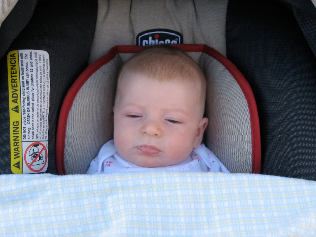 Ein Baby unter einer Babywiege mit einem Warnaufkleber auf der linken Seite der Wiege.