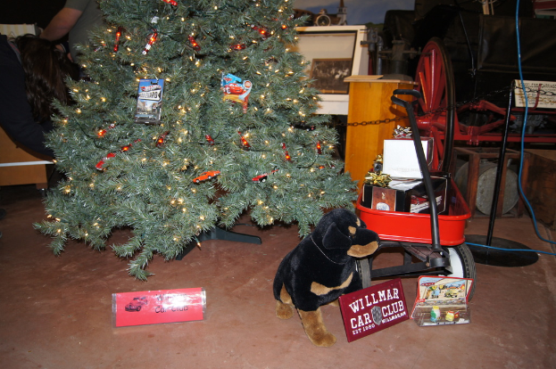 Ein Hundespielzeug, Namensschilder, ein Einkaufswagen mit Gegenständen, ein Weihnachtsbaum, ein Rad, ein Pfahl, eine Kette, eine Holzplatte, eine Person und diverse weitere Gegenstände im Hintergrund.