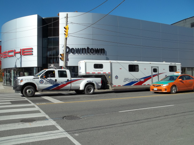 Ein Polizeiauto vor einem Gebäude mit Text geparkt, mit einem Verkehrssignal im Vordergrund und Bäumen und einem klaren blauen Himmel im Hintergrund.