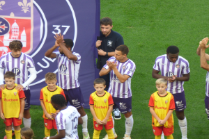 Eine Gruppe junger Jungs steht auf einem Fußballfeld, klatscht in die Hände mit einem Banner und Logos im Hintergrund.