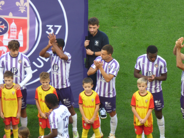 Eine Gruppe junger Jungs steht auf einem Fußballfeld, klatscht in die Hände mit einem Banner und Logos im Hintergrund.