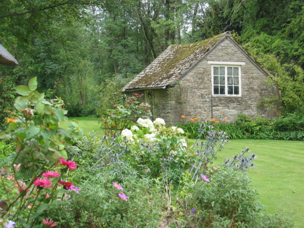 Ein Haus umgeben von Pflanzen und Bäumen auf einer grünen Fläche.