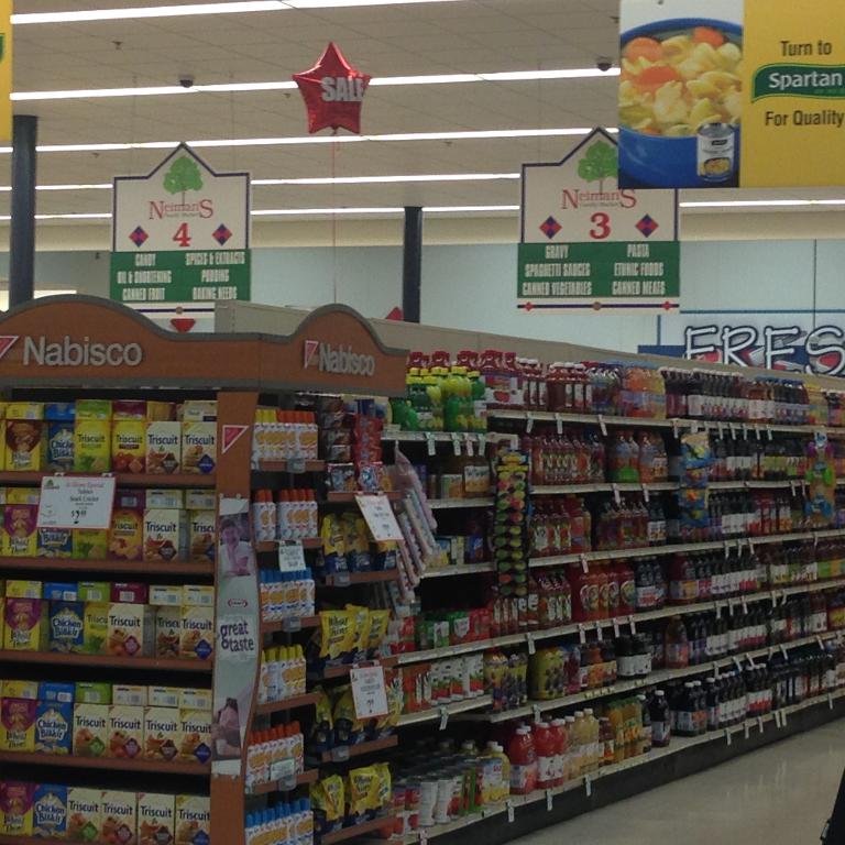 Ein Supermarktinneres mit Regalen voller Lebensmittel, Deckenlampen und Schildern.