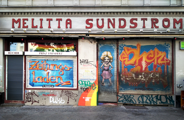 Ein Gebäude mit Graffiti, Rollläden und Schildern mit Text, beleuchtet von Lampen, mit einer Straße unten.