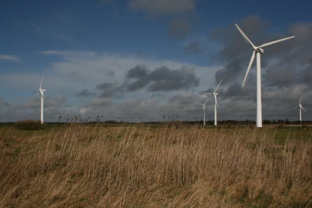 Ein Feld von Windkraftanlagen in einer grünen Landschaft mit Bäumen im Hintergrund und Wolken am Himmel, mit Text, der den Standort als Niederlande angibt.