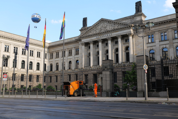 Großes modernes Gebäude mit vielen Fenstern, identifiziert als der Bundestag in Berlin, Deutschland, umgeben von Straßeninfrastruktur, Füßgängern und Bäumen unter einem bewölkten Himmel.