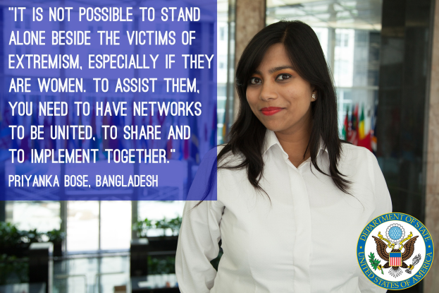 Eine Frau in einem weißen Hemd steht vor einem Gebäude mit einer Inschrift über die Unterstützung von Opfern des Extremismus, mit einem Logo in der rechten unteren Ecke.