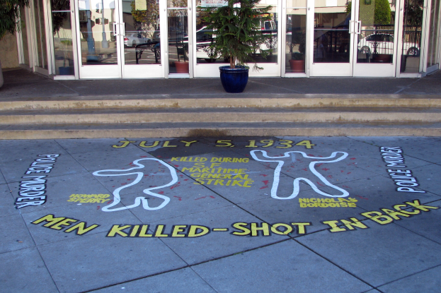 Ein Gebäude mit Glastüren und Fenstern, eine Topfpflanze und ein Gehwegschild mit der Aufschrift "Männer getötet, erschossen im Rücken."