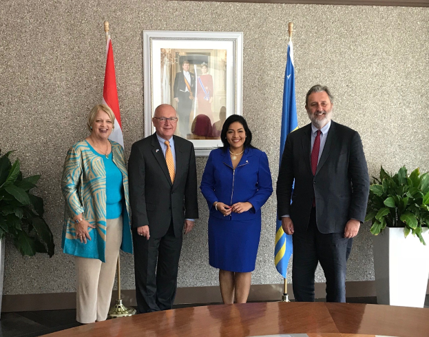 Gruppe von Menschen, die um einen Tisch mit Papieren stehen, umgeben von Fahnen, Topfpflanzen und einem gerahmten Foto an der Wand, was die Unterzeichnung eines U.S.-Kanada-Memorandums von Verständnis anzeigt.