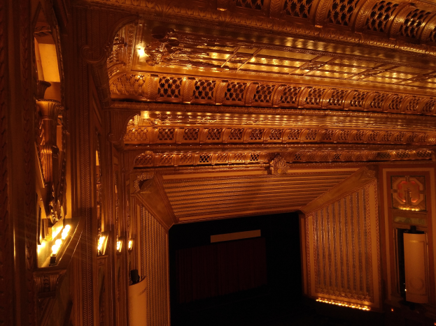 Ein prächtiges Theaterinnere mit dunklem Hintergrund, beleuchtet von beiden Seiten, mit einer kunstvoll gestalteten Decke.