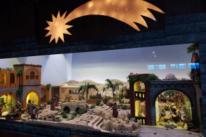 Eine Krippe-Ausstellung im Museum mit Figuren, Tieren, Gebäuden und Grünpflanzen, beleuchtet von oben.