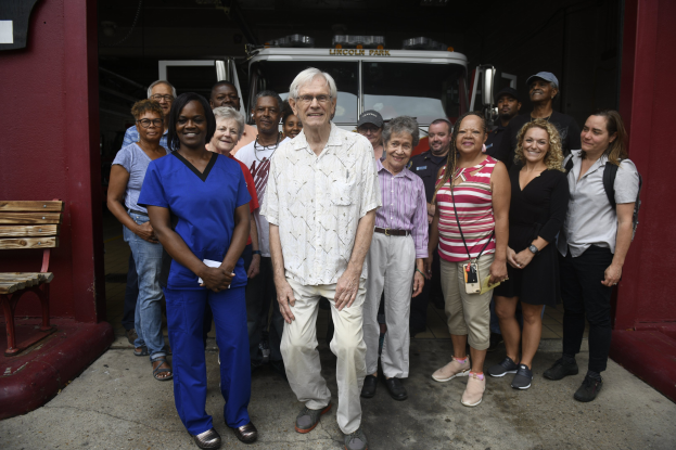 Eine Gruppe von Freiwilligen vor einem Feuerwehrauto mit einer Bank auf der linken Seite und einer Wand im Hintergrund.