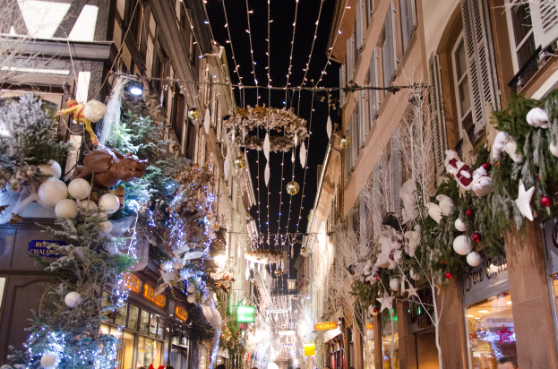 Ein lebendiger Weihnachtsmarkt in Straßburg, Frankreich, mit Menschen, die zwischen Gebäuden mit Weihnachtsbäumen, Lichtern und anderen festlichen Dekorationen unter einem sichtbaren Himmel spazieren.