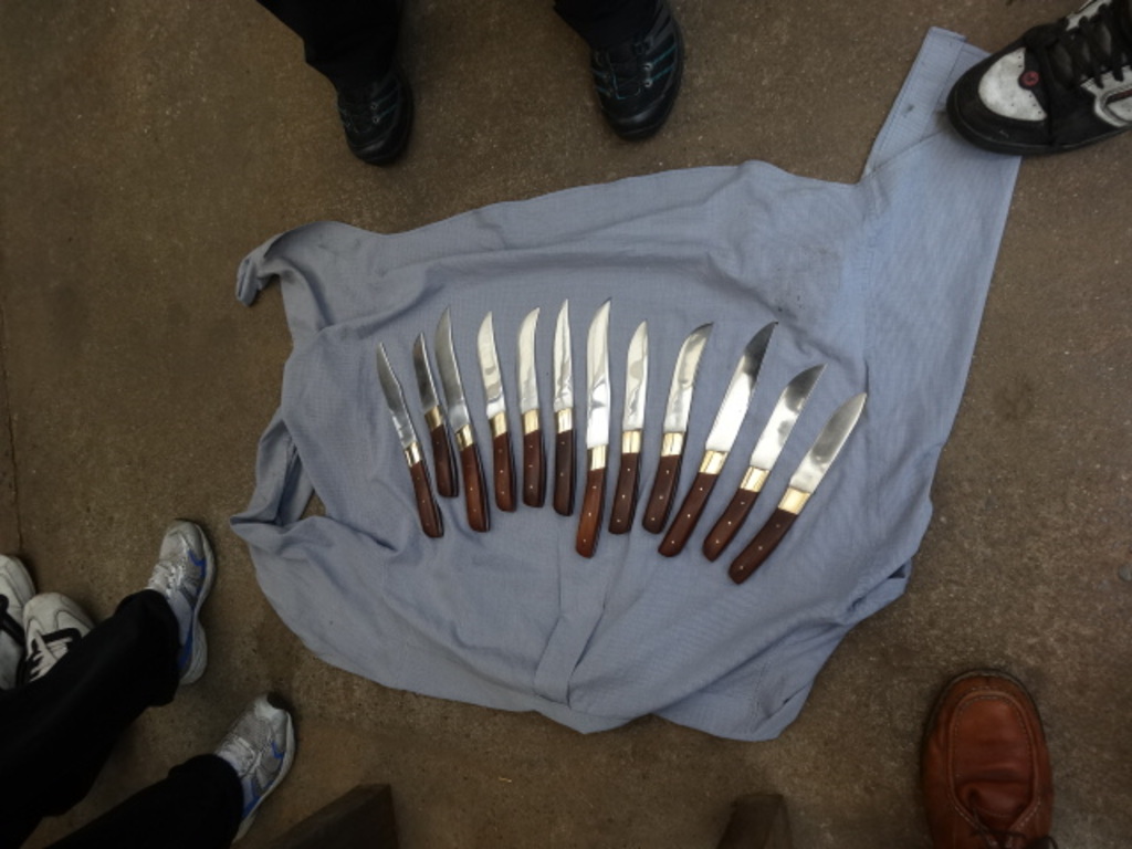 Ein Tuch auf einer Straße, die mit vielen Messern bedeckt ist, mit zahlreichen Personenbeinen drumherum.