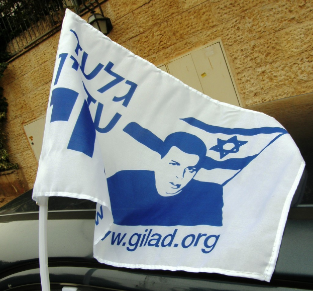 Ein Fahrzeug ist auf einer Straße in der Nähe eines Gebäudes mit einer Flagge, einem Zaun und einer Straßenlaterne geparkt.