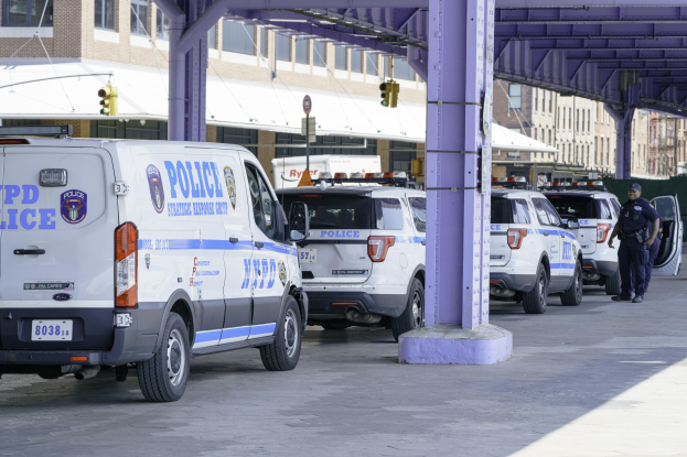 Eine Gruppe von Polizeiwagen steht am Straßenrand mit einer Person in der Nähe, Gebäude, Pfosten, Verkehrszeichen und eine Brücke im Hintergrund.