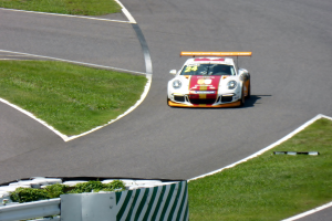 Ein Porsche 911 GT3 RSR auf der Nürburgring 24 Stunden Rennstrecke, umgeben von grünem Gras und einem Geländer, mit dem auffälligen Design und der schlanken Form des Autos.