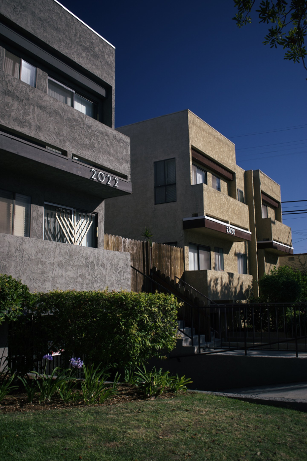 Eine Reihe von Wohngebäuden in San Francisco, Kalifornien, mit sichtbaren Fenstern, Grünflächen, einem Zaun, Treppen, einem Baum, Oberleitungen und einem Himmel als Hintergrund.