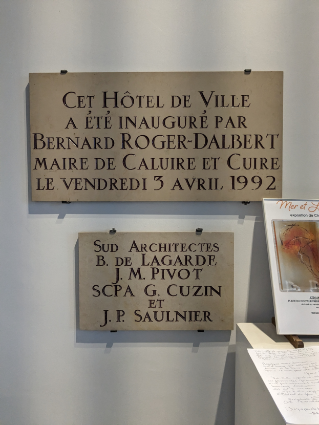 Eine Wand mit einer Plakette, die "Cet Hotel de Ville" und ein Foto auf einem Ständer daneben.