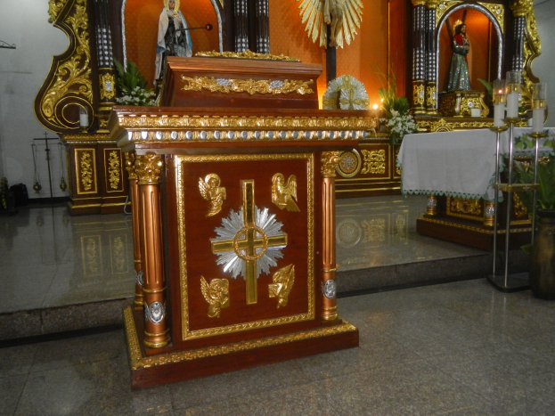 Ein Altar in einer Kirche mit einem Kreuz, Statuen, Blumensträußen, Kerzen, einem Tisch mit einer Decke und anderen Gegenständen, während die Wände mit Lichtern geschmückt sind.