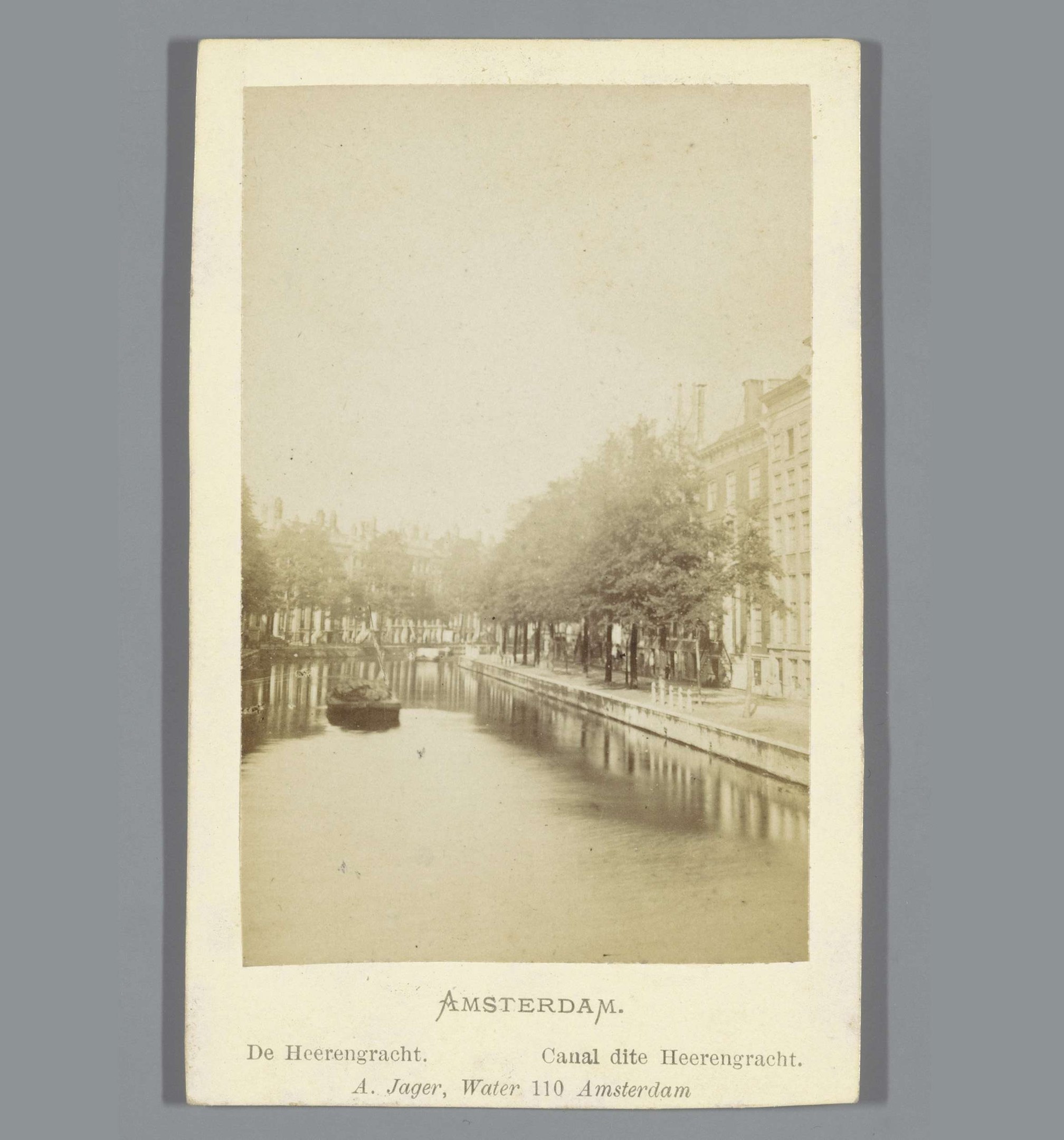 Schwarz-weiß-Foto eines Kanals in Amsterdam mit einem Boot, Bäumen am Ufer und Gebäuden im Hintergrund, mit Text unten.