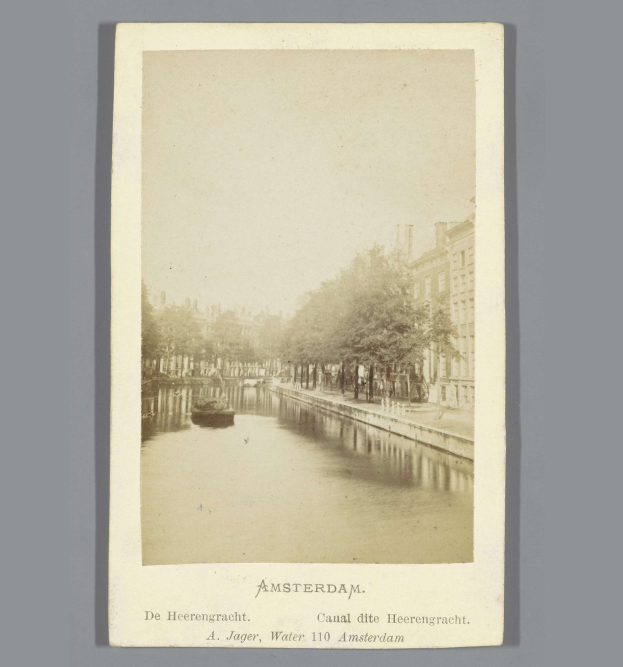 Schwarz-weiß-Foto eines Kanals in Amsterdam mit einem Boot, Bäumen am Ufer und Gebäuden im Hintergrund, mit Text unten.