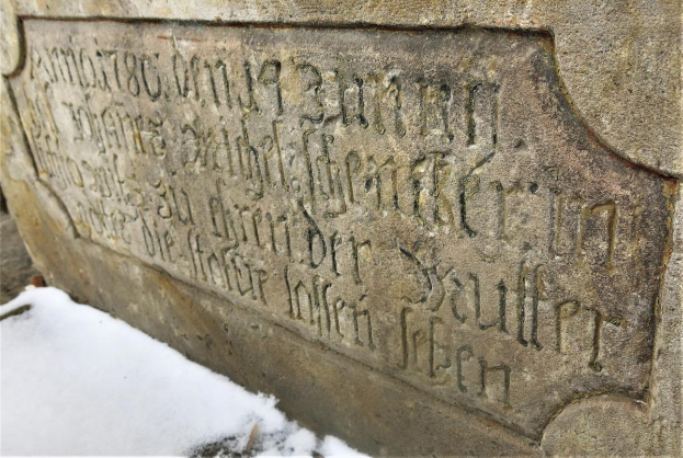Ein steinerner Gedenkstein an einem Gebäude, bedeckt von Schnee, mit Text, der wahrscheinlich Holocaust-Opfer gedenkt.