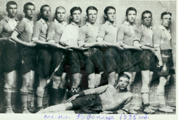 Ein Schwarz-Weiß-Foto einer Fussballmannschaft mit einem Mann in der Mitte auf dem Boden liegend und Text unten.