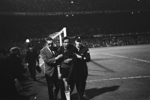 Schwarzes Bild von Fußballspielern, die auf einem Feld mit einem Torpfosten und einer beleuchteten Zuschauertribüne feiern.