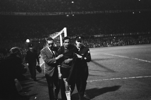 Schwarzes Bild von Fußballspielern, die auf einem Feld mit einem Torpfosten und einer beleuchteten Zuschauertribüne feiern.