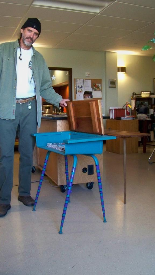 Ein Mann, der steht und den oberen Teil eines Studiertisches hält.