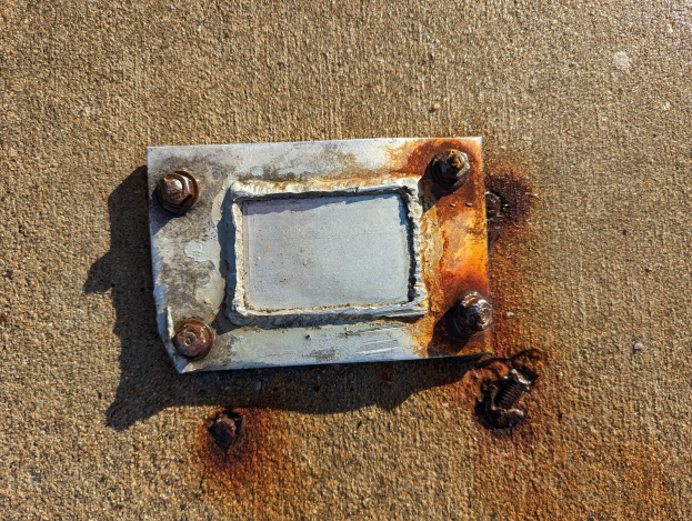 Ein verrostetes Metallblech liegt auf dem Boden mit ein paar verstreuten Schrauben drumherum.