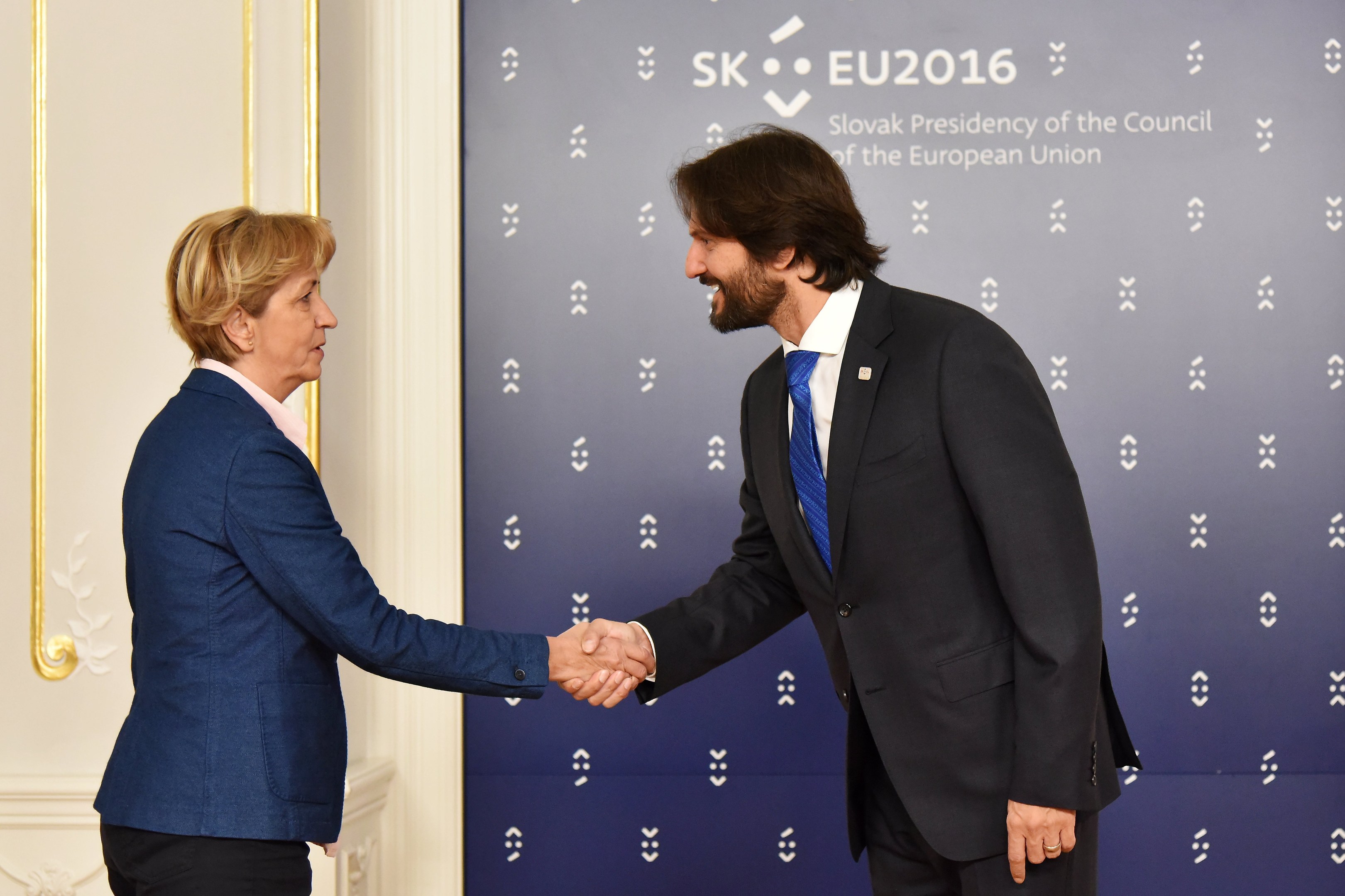 Bundeskanzlerin Angela Merkel und Bundespräsident Joachim Gauck schütteln sich die Hände vor einem "EU-Gipfel"-Plakat, beide lächeln.